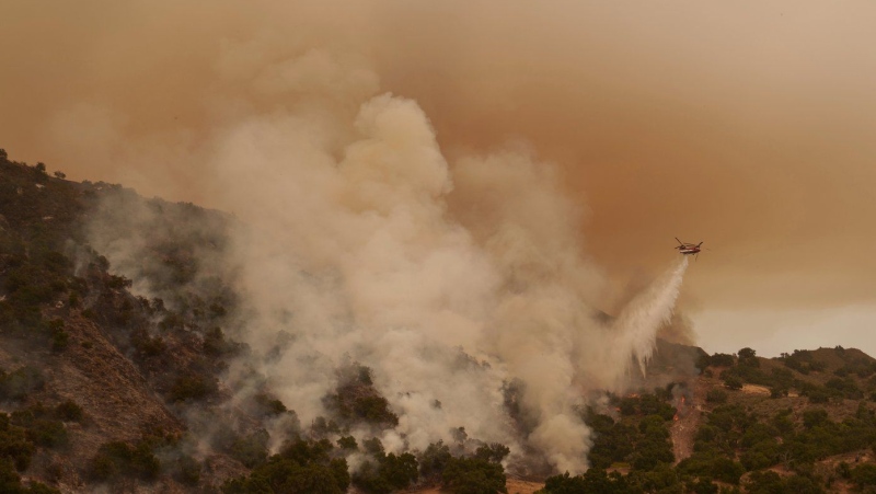 A water-dropping helicopter drops on flames from the advancing Lake Fire in Los Olivos, Calif., Saturday, July 6, 2024. (AP Photo/Eric Thayer)