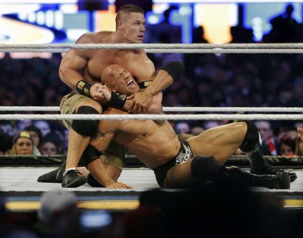 Wrestler John Cena, top, chokes Dwayne Douglas Johnson, known as The Rock, as they wrestle, April 7, 2013, in East Rutherford, N.J., during Wrestlemania. Cena announced Saturday, July 6, 2024, that he will retire from professional wresting next year after two decades in the ring. (AP Photo/Mel Evans, File)